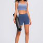 Model in a seamless blue sports bra and shorts, holding a workout mat, ready for a fitness session.