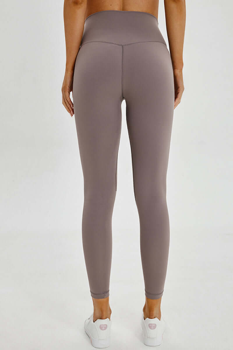 Model showcasing the back view of Millennia wide seamless band waist sports leggings in a stylish taupe color.