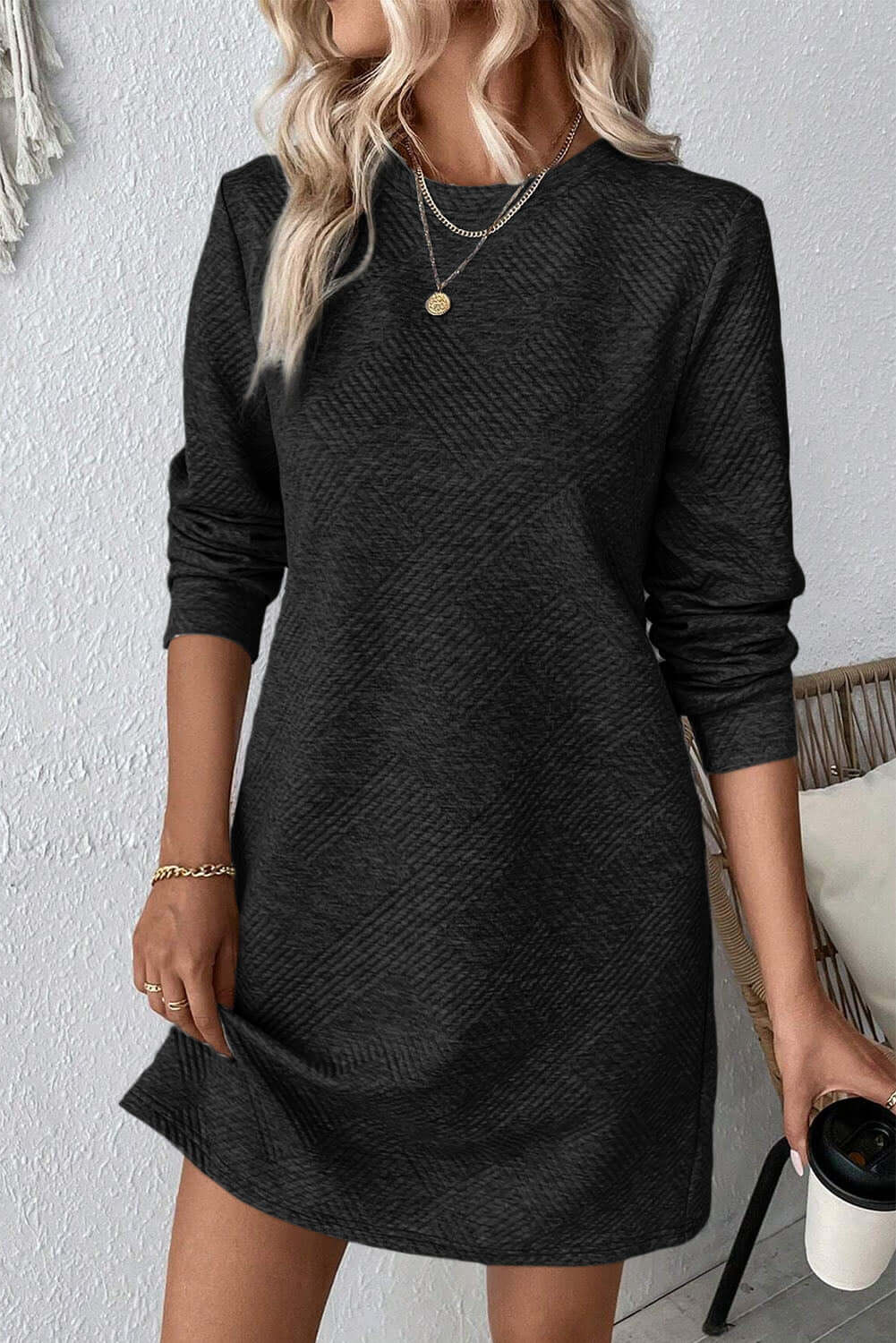 Woman wearing a Bella Road textured round neck long sleeve mini dress in black, styled with necklaces and holding a cup.