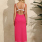 Woman in a backless tassel surplice spaghetti strap cover-up dress in hot pink standing in front of a textured wall.