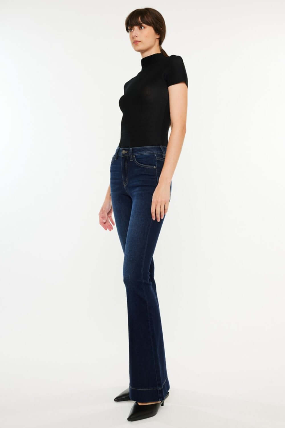 Model wearing Kancan High Rise Slim Flare Jeans in dark wash, paired with a fitted black top and heels for a chic, polished look.