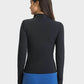 Back view of a woman wearing the Millennia Half Zip Thumbhole Sleeve Sports Top in black, paired with blue leggings.