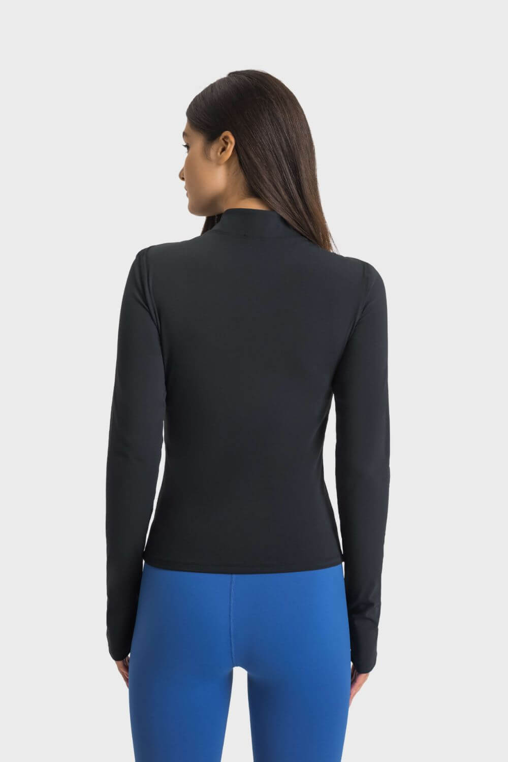 Back view of a woman wearing the Millennia Half Zip Thumbhole Sleeve Sports Top in black, paired with blue leggings.