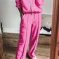 Woman wearing Bella Road Zip Up Long Sleeve Top and Pants Set in bright pink, standing in front of a mirror, showcasing trendy style and comfort.