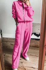 Woman wearing Bella Road Zip Up Long Sleeve Top and Pants Set in bright pink, standing in front of a mirror, showcasing trendy style and comfort.