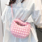 Pink quilted puffy crossbody bag with removable strap worn over a white shirt.