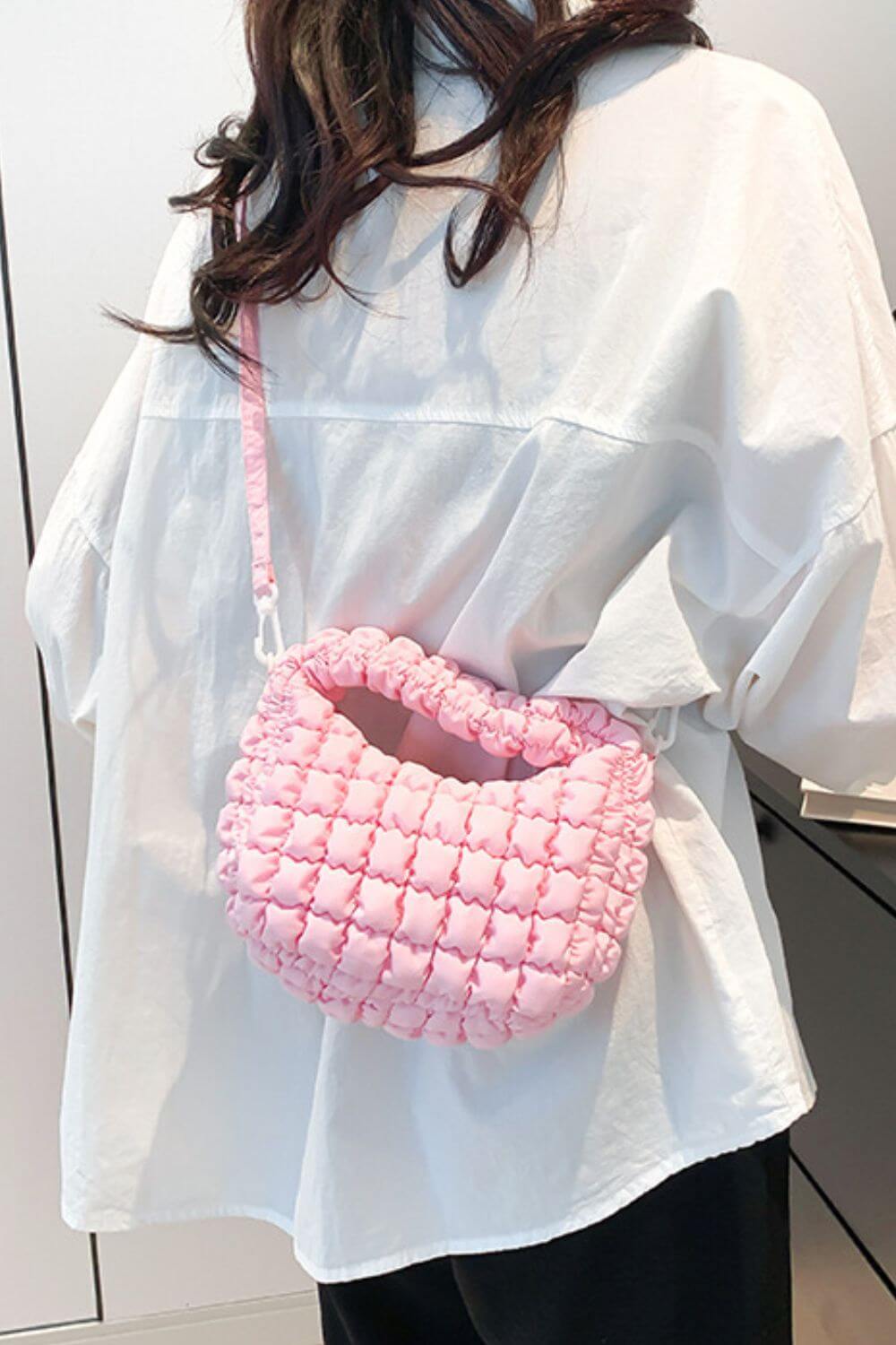 Pink quilted puffy crossbody bag with removable strap worn over a white shirt.