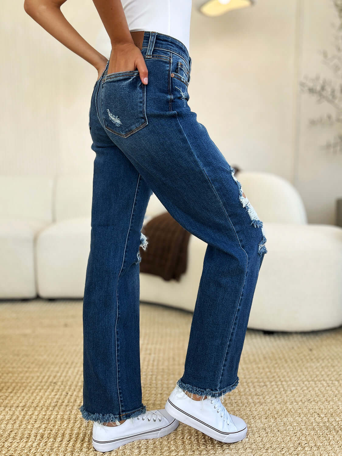 Woman wearing Judy Blue Full Size Mid Rise Distressed Raw Hem Jeans with white sneakers, showcasing the trendy raw hem and distressed detailing.