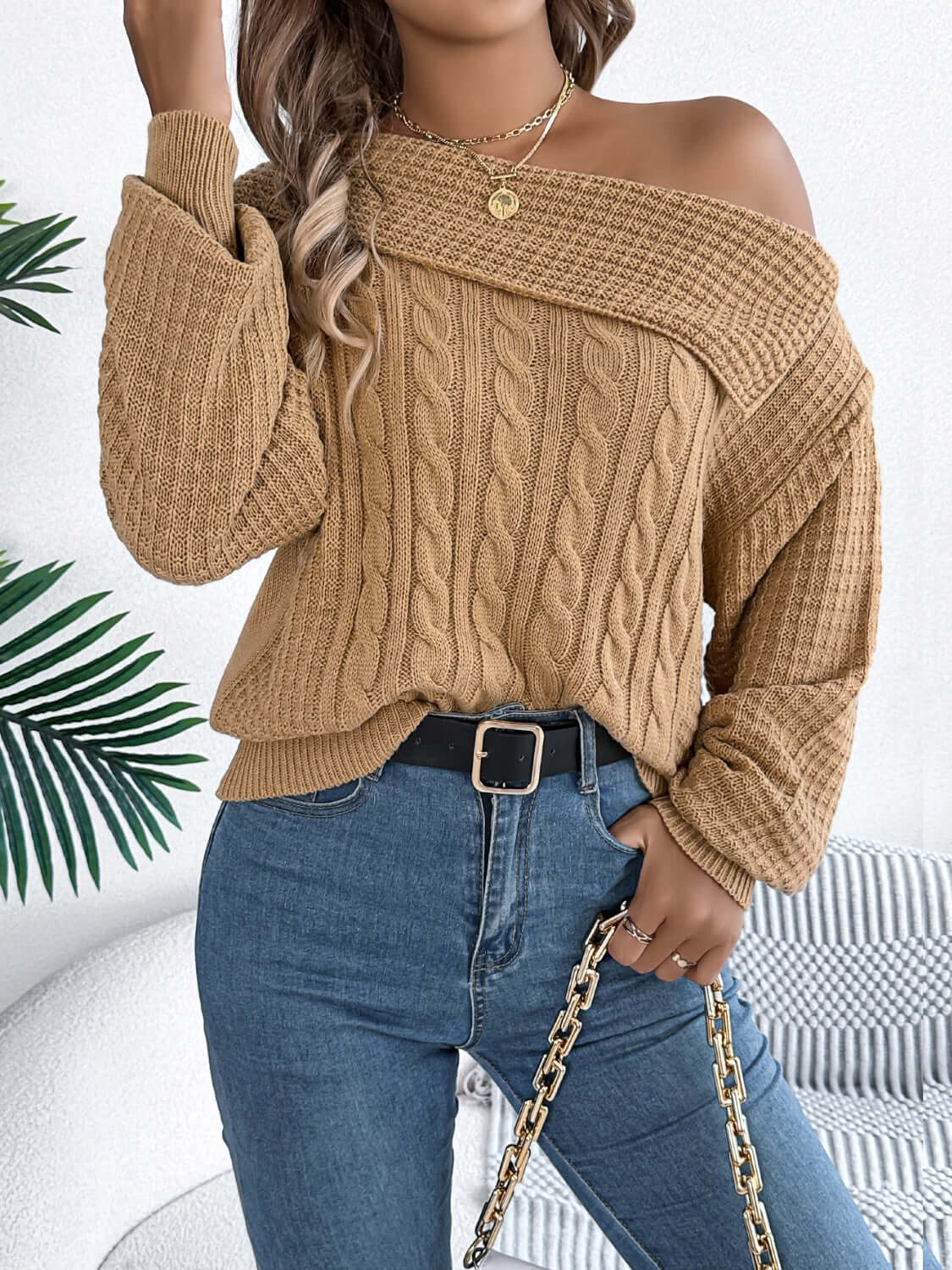 Woman wearing Bella Road Cable-Knit One Shoulder Long Sleeve Sweater in beige, paired with jeans and accessories, standing in stylish setting.