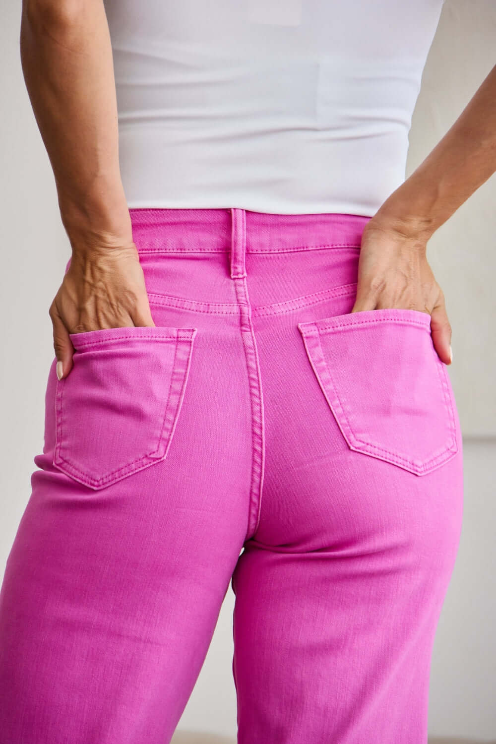 Close-up of back view of woman wearing pink high-waisted jeans with raw hem, showcasing tummy control and flattering fit. RFM Jeans.