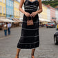 Woman in stylish black openwork spaghetti strap cover-up, holding a mini bag, walking on a charming street.