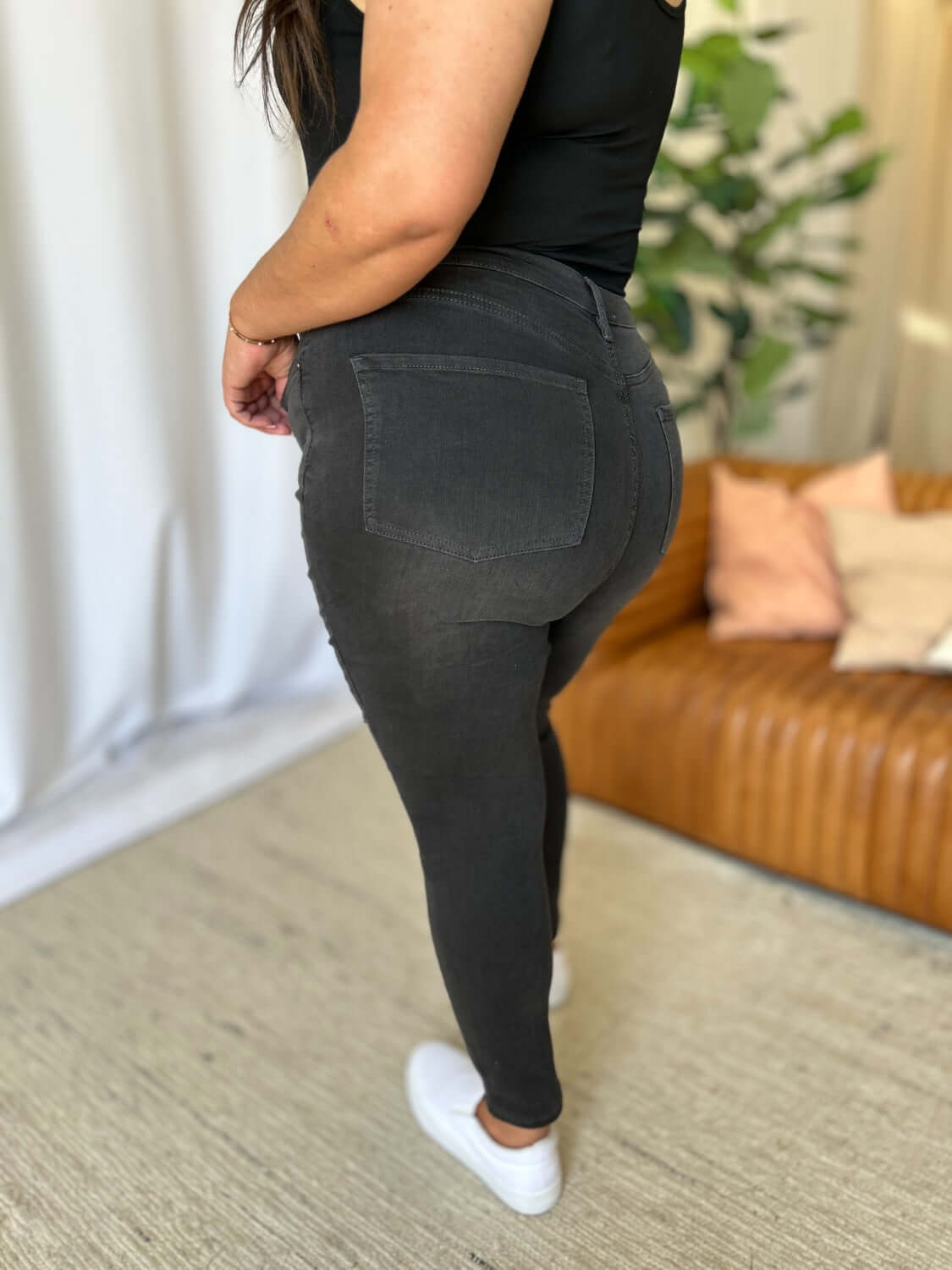 Woman wearing RFM Full Size High Rise Tummy Control Skinny Jeans in black, highlighting figure-hugging fit and high-waist design.