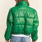 Woman wearing green faux leather cropped puff jacket with turtleneck and drawstring hem, paired with denim shorts.