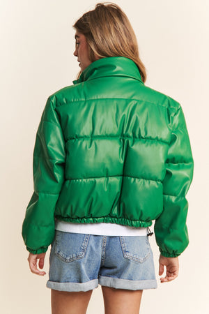 Woman wearing green faux leather cropped puff jacket with turtleneck and drawstring hem, paired with denim shorts.