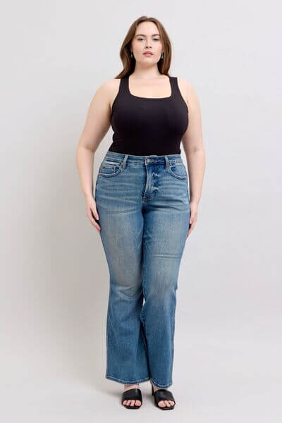 Model showcasing Judy Blue Mid Rise Tummy Control Vintage Wash Jeans with a black tank top and stylish sandals.