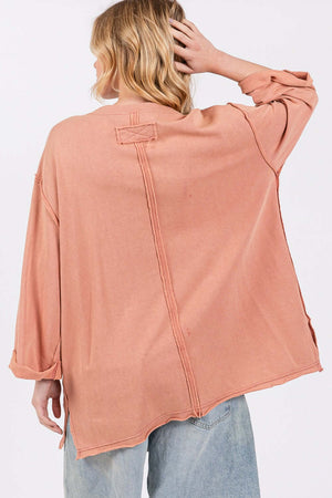 Woman wearing a loose-fitting peach-colored shirt with raw edges, seen from the back.