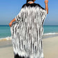 Woman wearing slit tie-dye half sleeve cover up on a beach with ocean waves in the background.