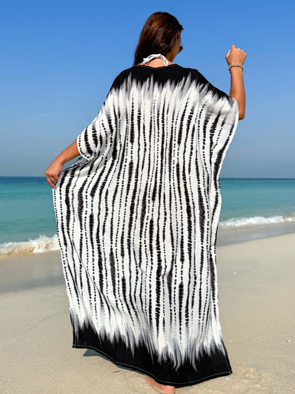 Woman wearing slit tie-dye half sleeve cover up on a beach with ocean waves in the background.