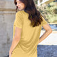 Woman wearing Basic Bae Bamboo V-Neck Short Sleeve T-Shirt in yellow, shown from the back, paired with jeans in an outdoor setting.