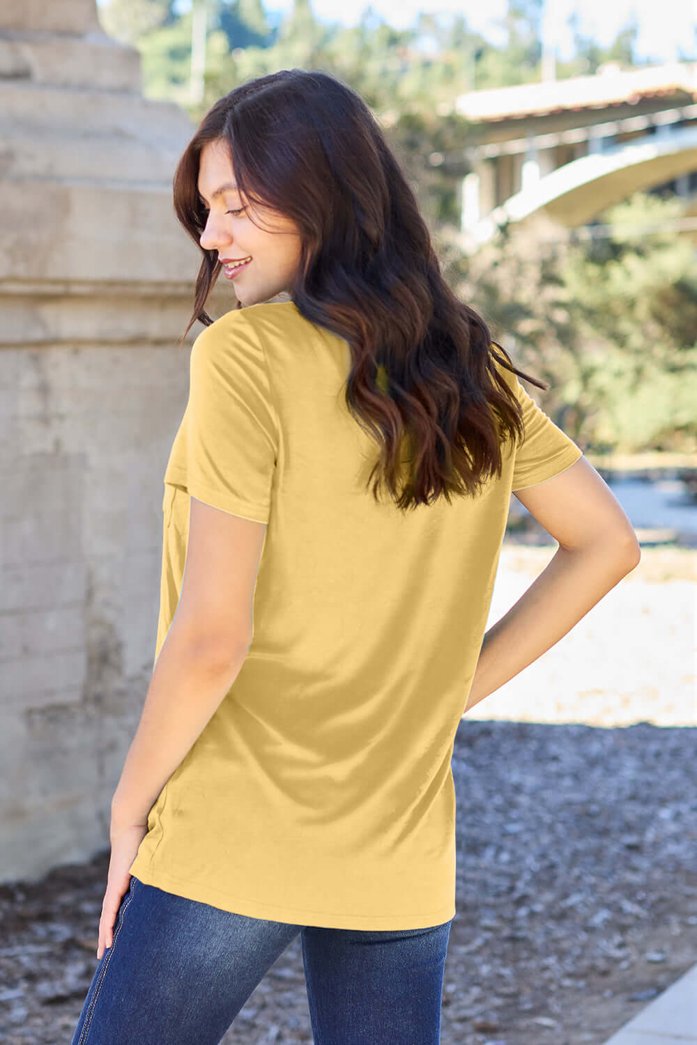 Woman wearing Basic Bae Bamboo V-Neck Short Sleeve T-Shirt in yellow, shown from the back, paired with jeans in an outdoor setting.