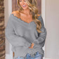 Woman wearing Bella Road frayed hem dropped shoulder sweater in grey, smiling indoors.