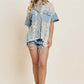 Woman wearing a Button Up Short Sleeve Lace Shirt with a delicate lace design and sophisticated button-up closure, paired with denim shorts and a hat