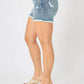 Woman wearing Button Fly Raw Hem Denim Shorts by Judy Blue Jeans, showcasing trendy raw hem detail and stylish summer look.