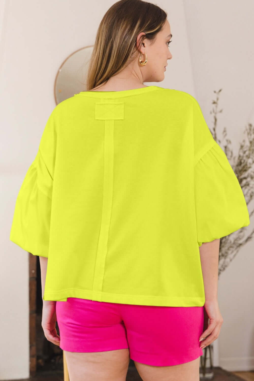 Woman wearing bright yellow oversized shirt and pink shorts, viewed from the back.