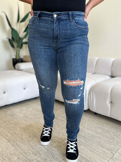 Woman wearing High Waist Distressed Skinny Jeans by Judy Blue featuring a flattering fit and distressed detailing in a modern living room.