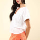 Woman wearing white notched short sleeve washed t-shirt and orange shorts with pockets, showcasing casual and stylish outfit.