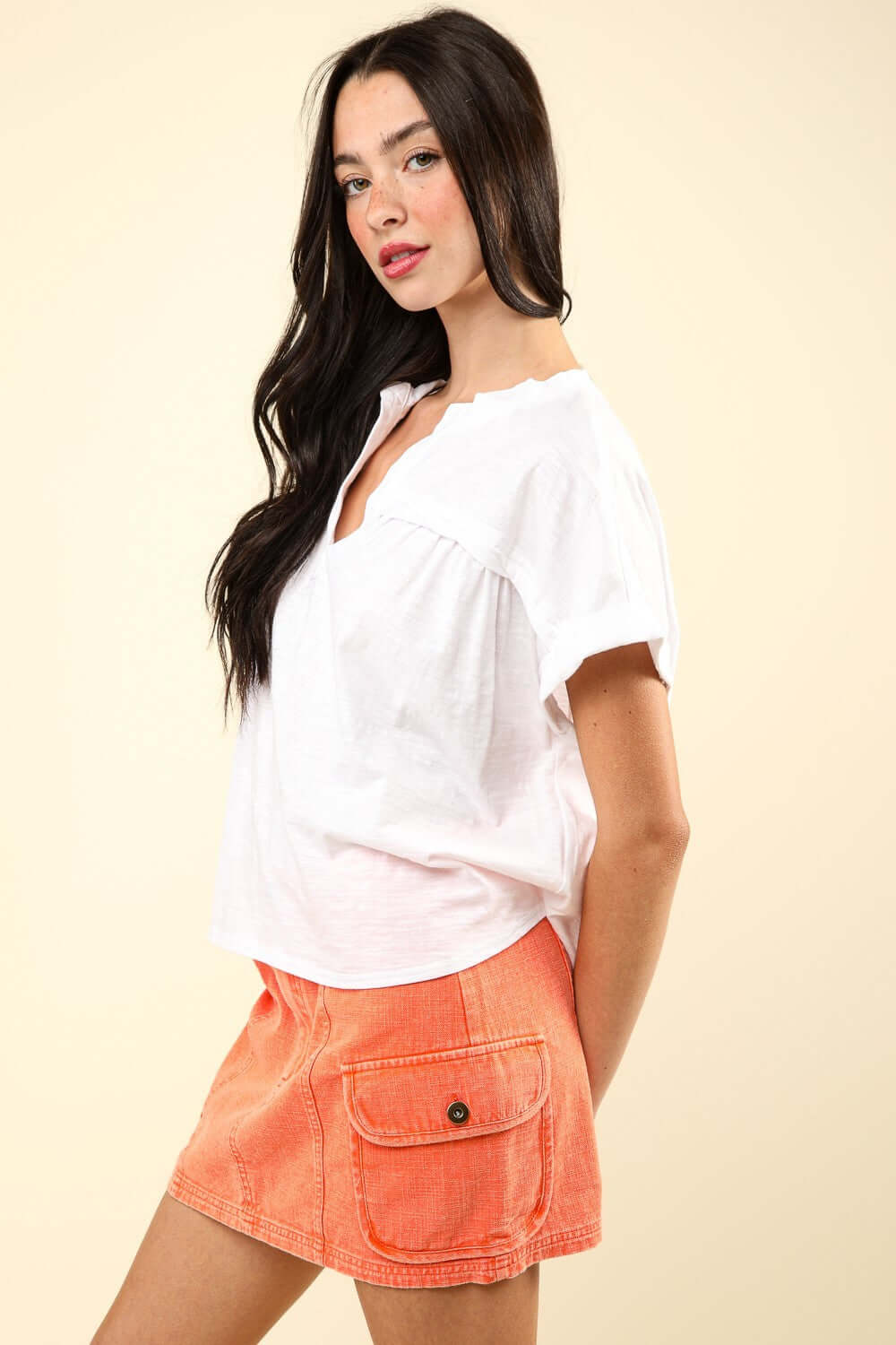 Woman wearing white notched short sleeve washed t-shirt and orange shorts with pockets, showcasing casual and stylish outfit.