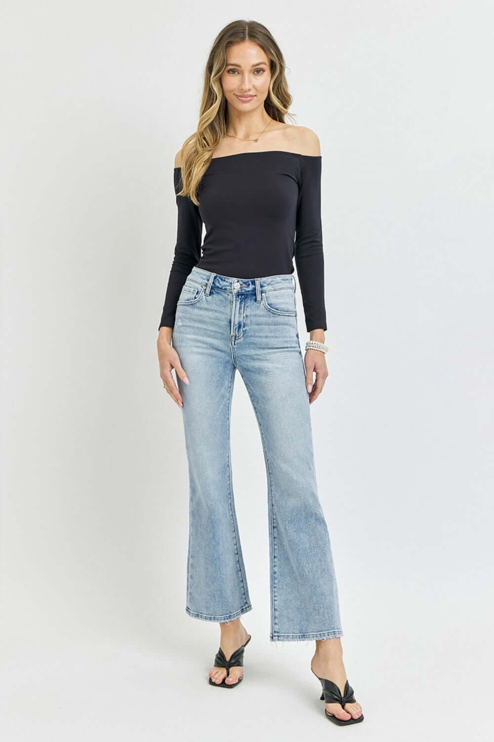 Woman wearing RISEN Full Size High Rise Ankle Flare Jeans with black off-shoulder top and black sandals.