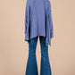 Woman wearing purple asymmetrical long sleeve top with drop sleeves, showing back view, paired with flared blue jeans.