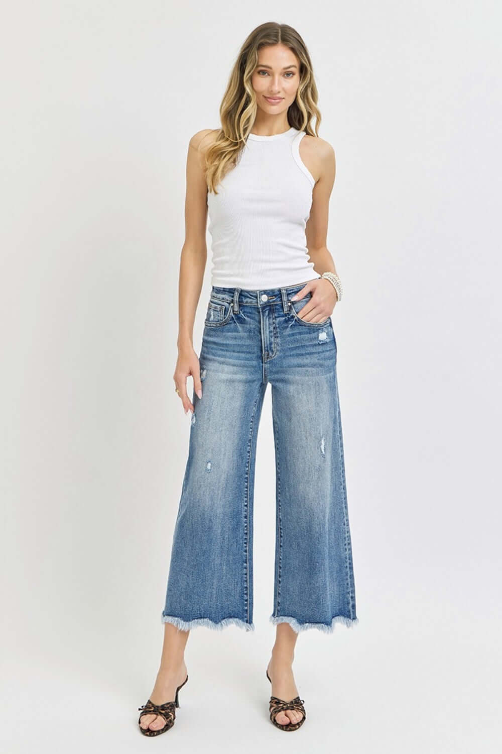 Woman wearing High Rise Cropped Flare Jeans from Risen Jeans, styled with a white tank top and sandals, showcasing the trendy denim look