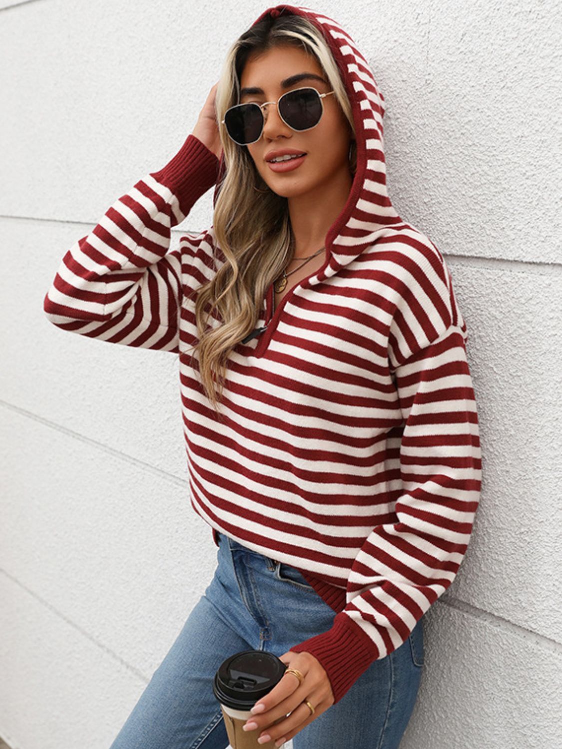 Woman wearing Perfee Striped Long Sleeve Hooded Sweater in burgundy, holding a coffee cup and looking stylish against a white wall.