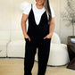 Woman wearing a bold black plunge sleeveless jumpsuit with pockets, standing in a stylish living room.