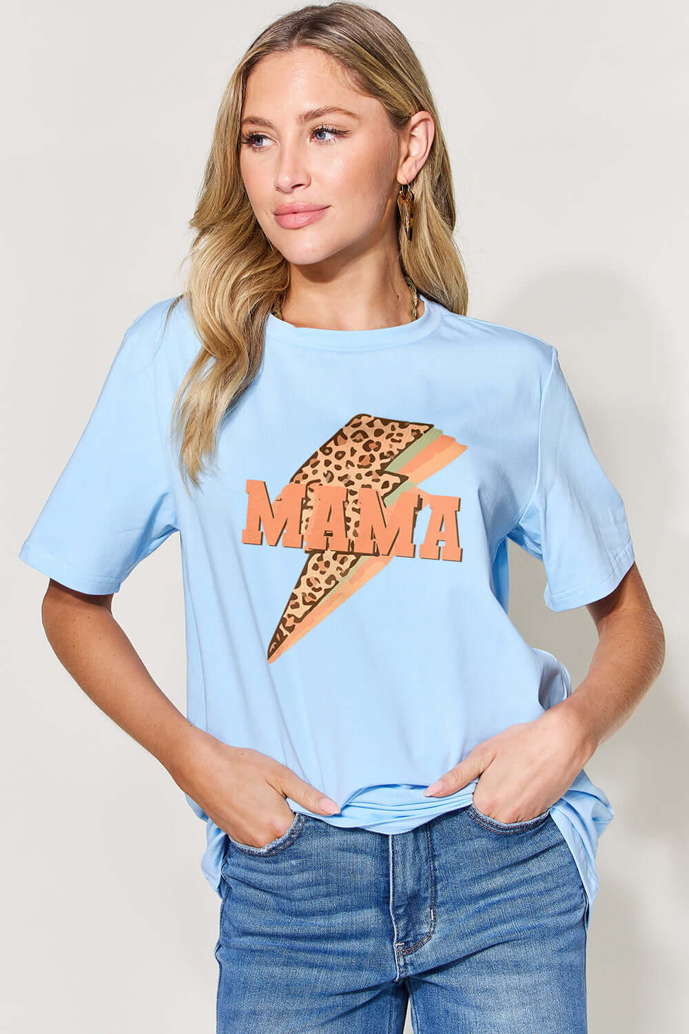 Woman wearing MAMA round neck short sleeve T-shirt in light blue with leopard print design, paired with blue jeans.