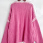 Pink open front cardigan with white contrast design, featuring a dropped shoulder and cozy style on a hanger.