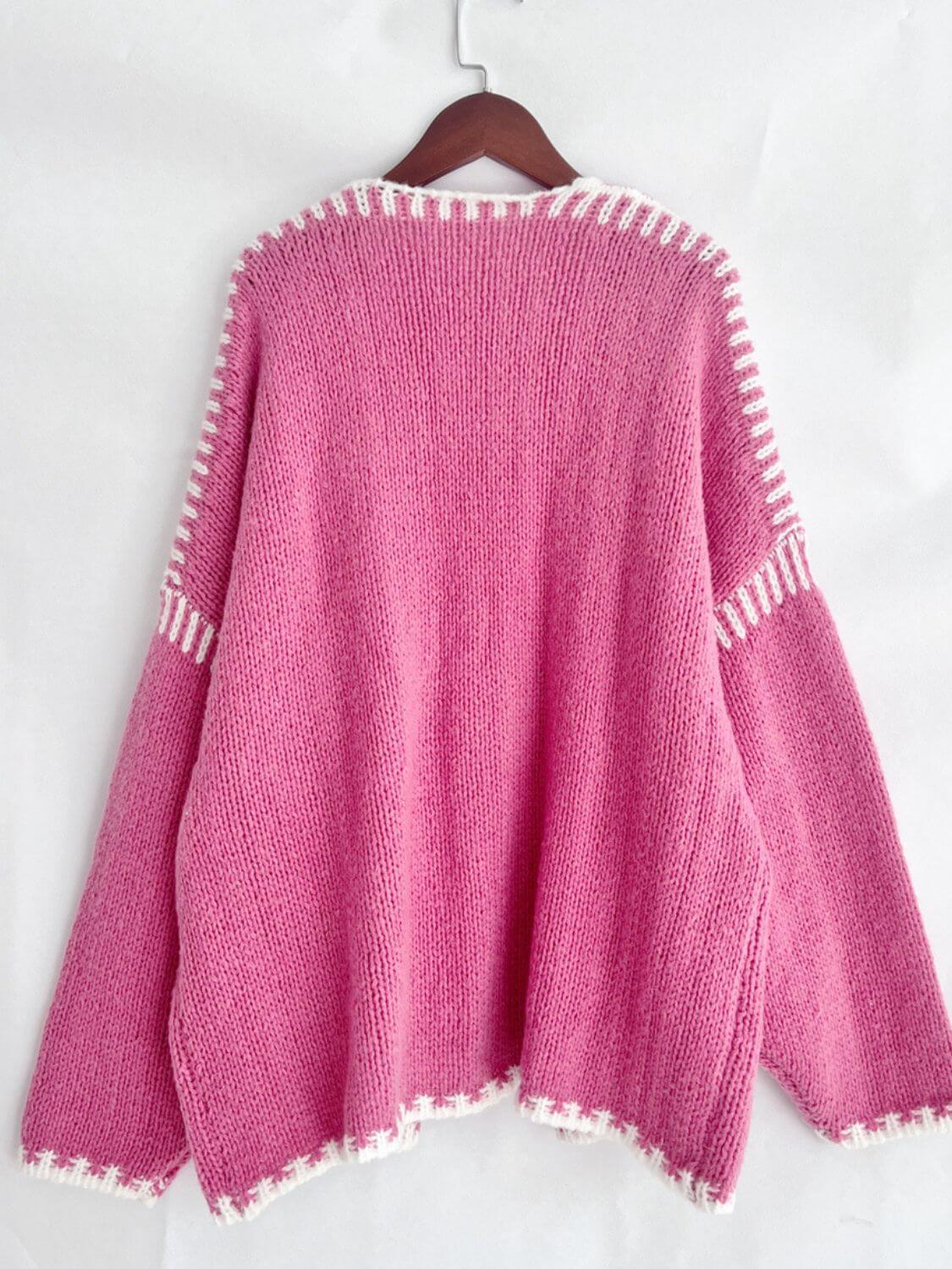 Pink open front cardigan with white contrast design, featuring a dropped shoulder and cozy style on a hanger.