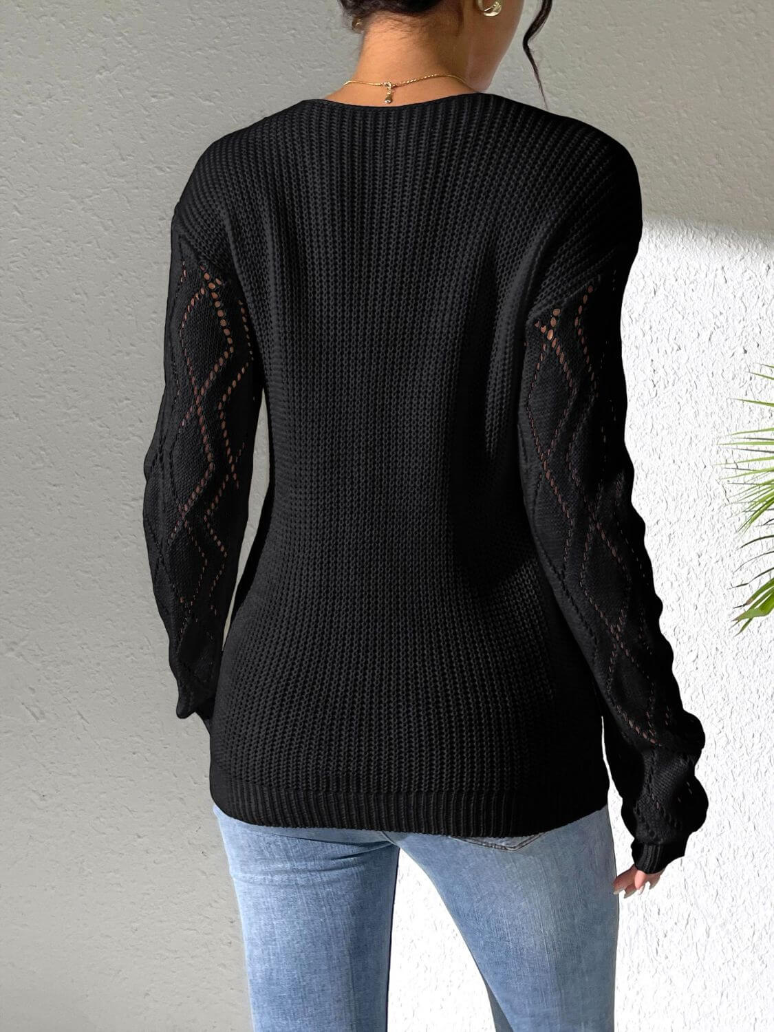 Woman wearing Bella Road Openwork V-Neck Long Sleeve Sweater in black, showcasing back design and stylish openwork sleeves.