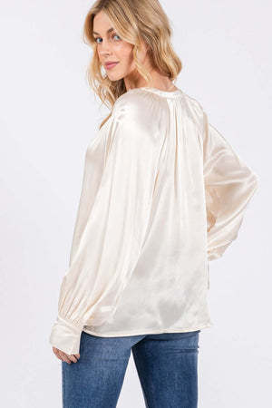 Woman wearing ivory-colored notched long sleeve blouse with raglan sleeves and split neckline, paired with blue jeans.