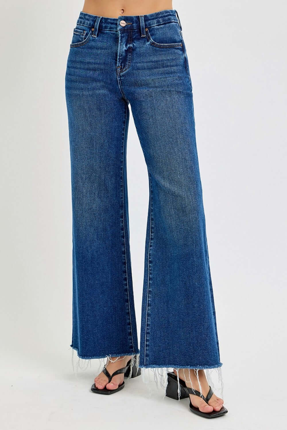 Risen tummy control high rise wide leg jeans with pockets and trendy frayed hem showcased with stylish black sandals.