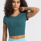 Woman wearing a cropped teal sports t-shirt with short sleeves, perfect for yoga and fitness activities.