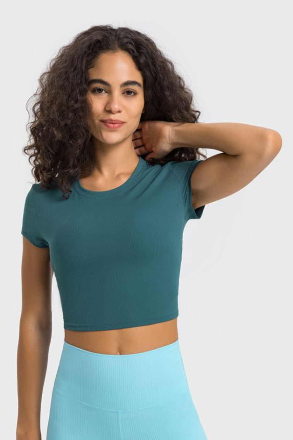 Woman wearing a cropped teal sports t-shirt with short sleeves, perfect for yoga and fitness activities.