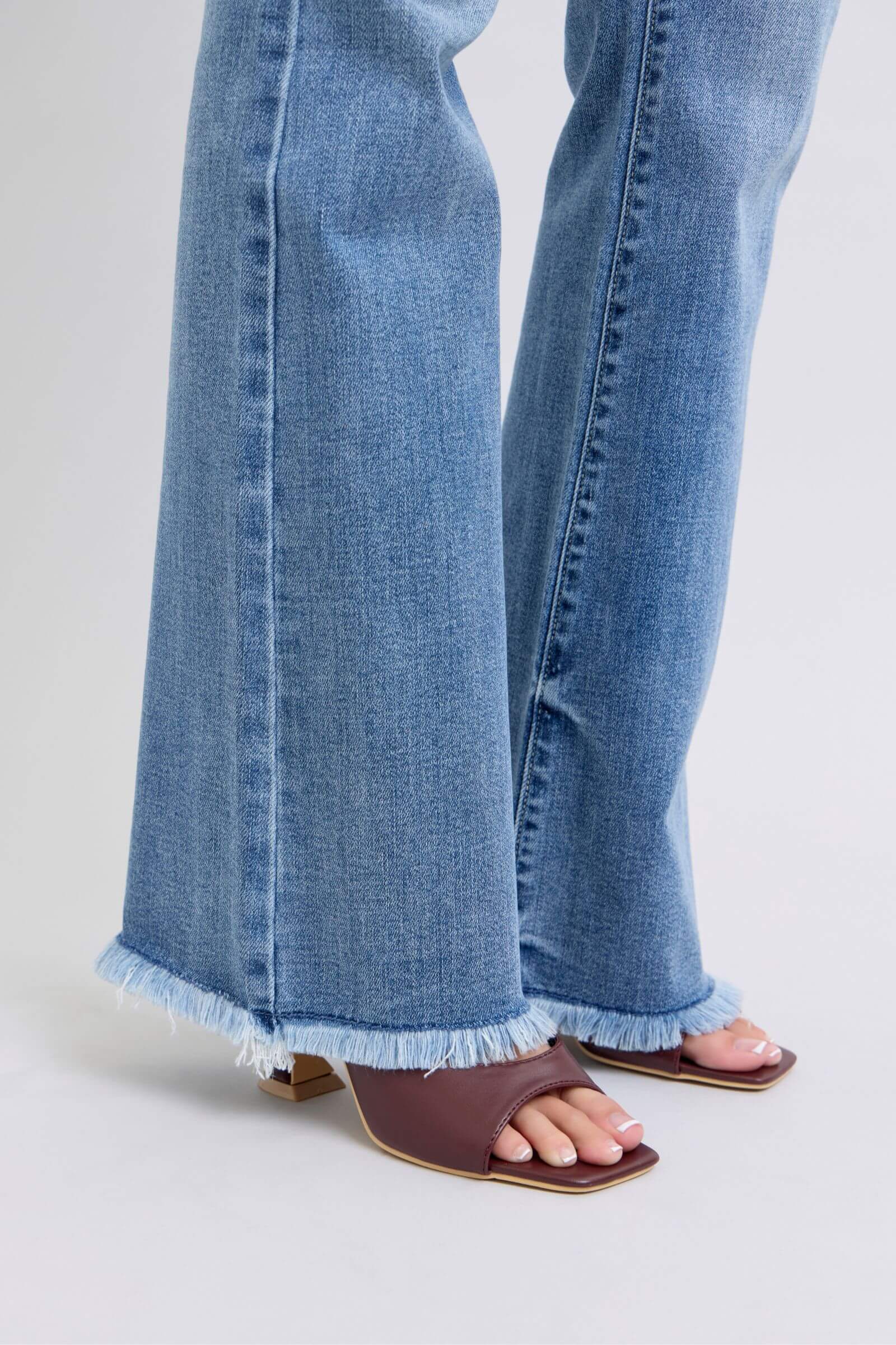 Trendy raw hem high rise bootcut jeans paired with stylish brown slide sandals, showcasing a chic casual look.