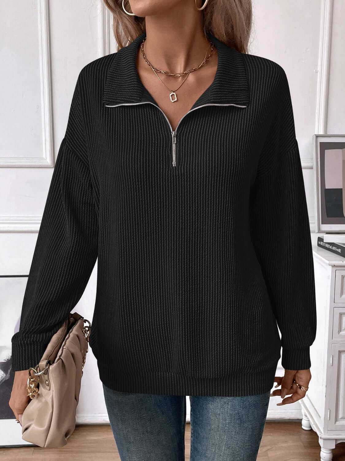 Woman wearing a black striped half zip long sleeve T-shirt with a casual style, paired with jeans and accessorized with a necklace and handbag.