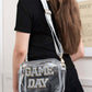 Transparent crossbody bag with "GAME DAY" letters, glitter trim, worn by woman, perfect for stadium events, adjustable strap.