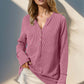 Woman wearing Double Take Full Size Notched Thumbhole Long Sleeve T-Shirt in pink, with buttoned neckline and thumbholes, standing against wall.