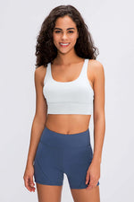 Model wearing Millennia Double X Sports Bra in white, paired with blue workout shorts, showcasing a stylish athletic look.