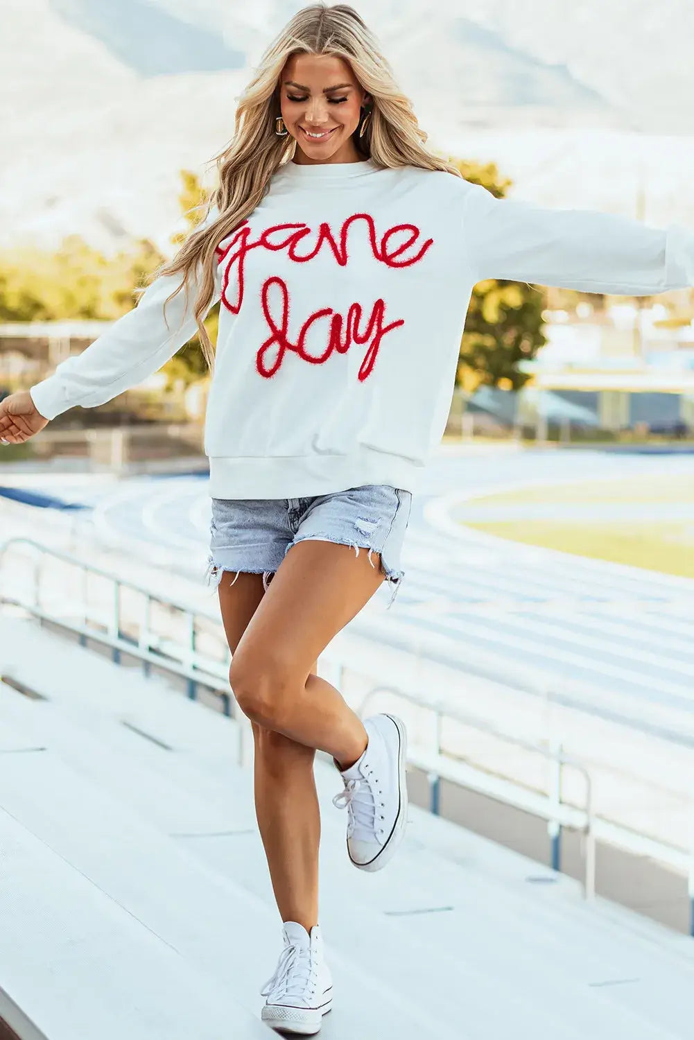 Woman wearing Bella Road Game Day Round Neck Long Sleeve Sweatshirt outdoors near a track.